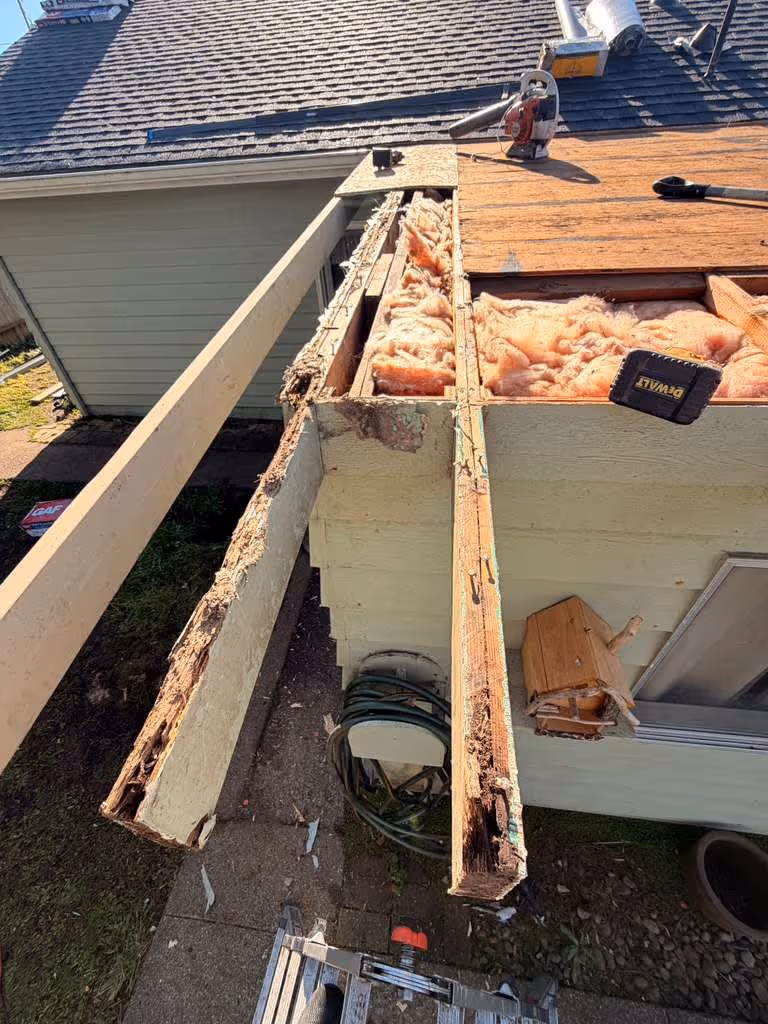 Partially removed wooden gutter with exposed pink insulation on the edge of a house roof during repair work.