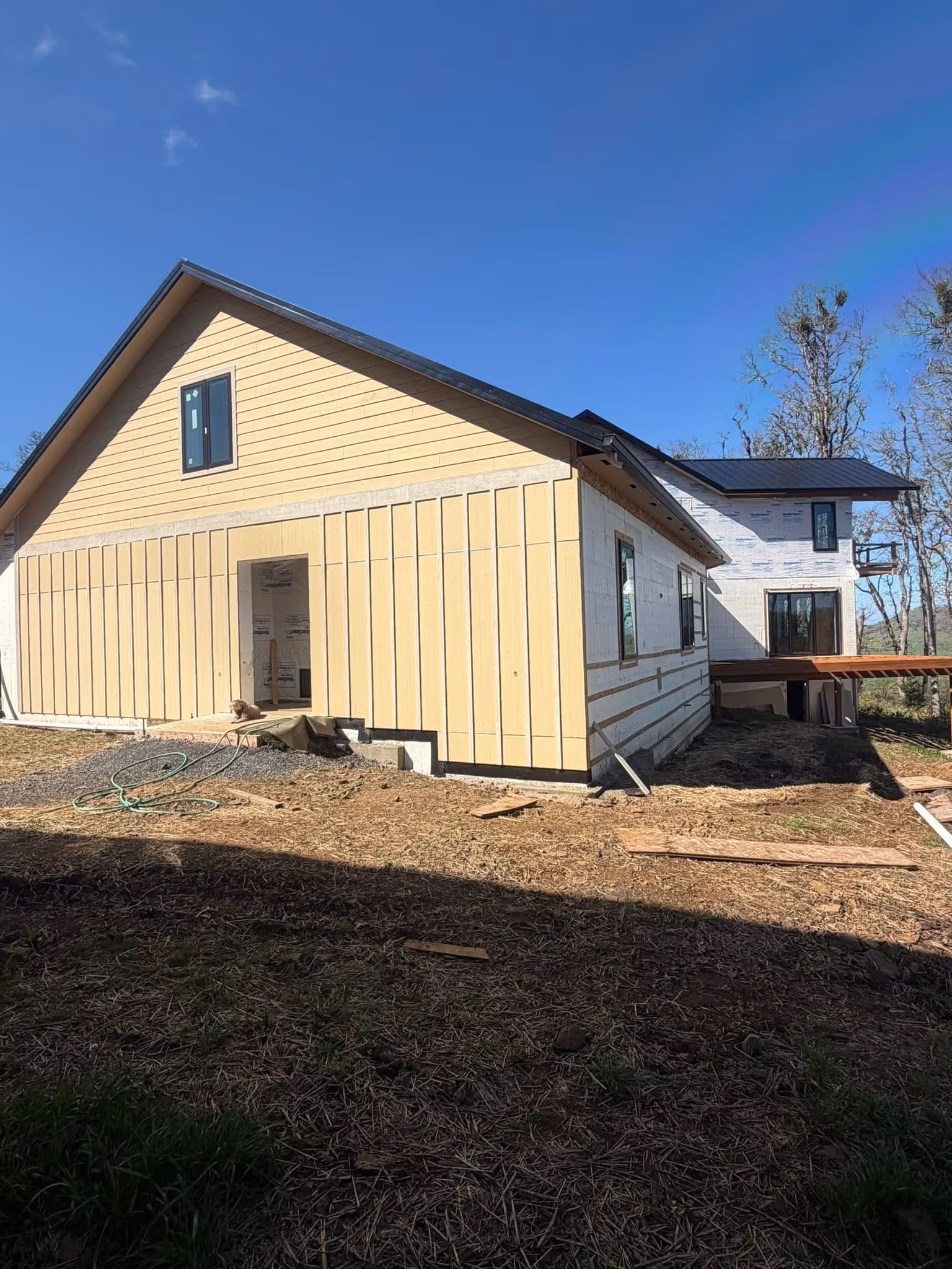 Partially constructed house with yellow siding on the front and white insulated walls on the side under a clear blue sky.