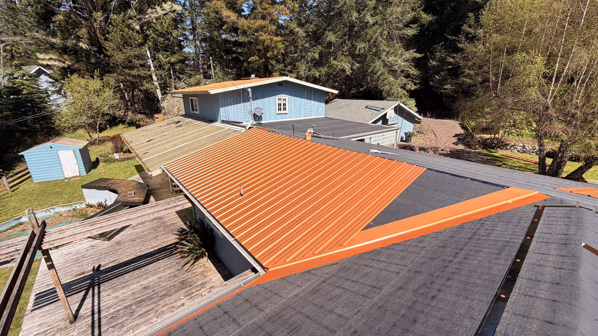 A house roof under construction with new corrugated metal panels partially installed and black roofing felt visible.