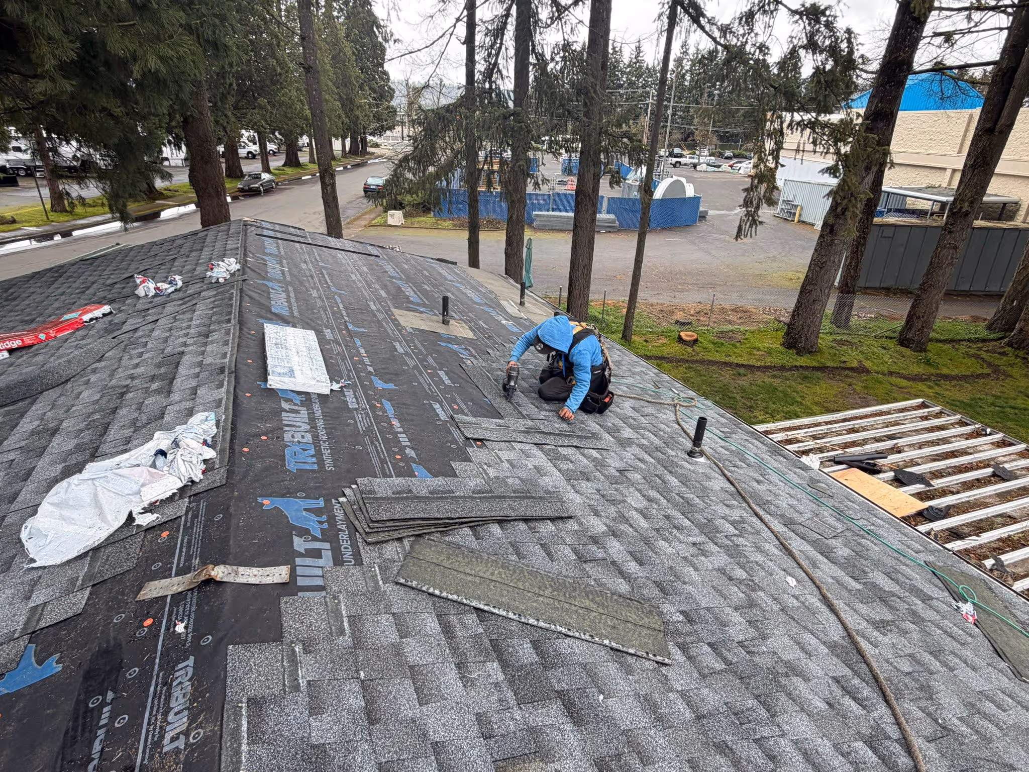 Roofer in a blue hoodie installing asphalt shingles on a residential roof underlayed with synthetic roofing felt.