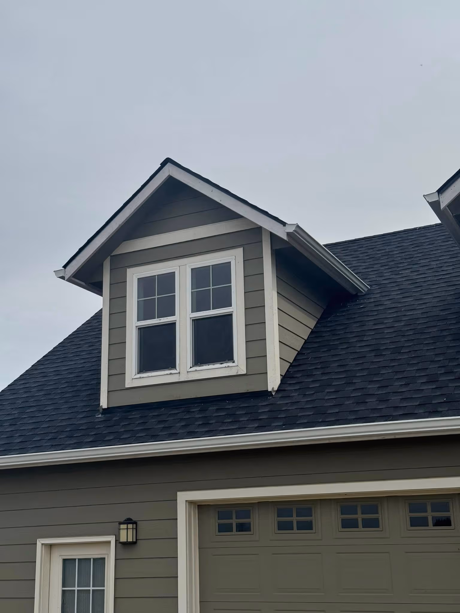 Grey house exterior showing a gable window above a garage door with small windows, under an overcast sky.