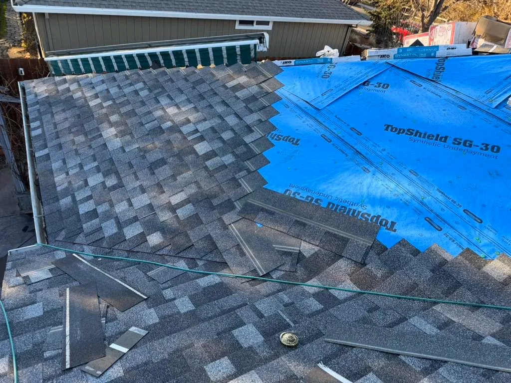 Partially completed roof with gray asphalt shingles installed on one section and blue synthetic underlayment on the other.