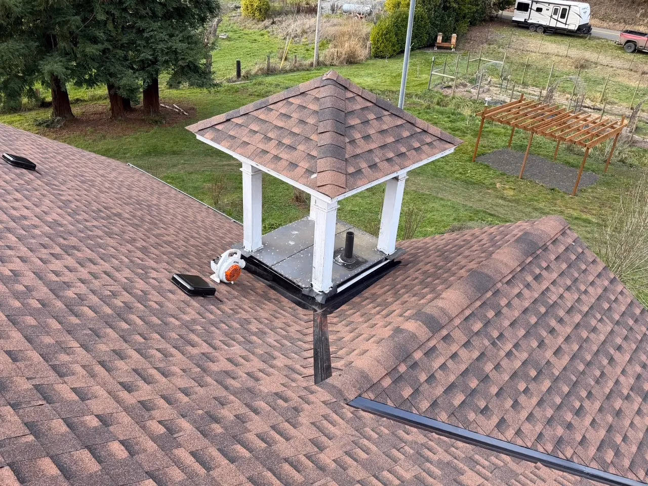 Brown shingled roof with a small white square cupola supported by four columns and a black vent pipe underneath.